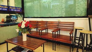 A seating area with wooden benches and tables, a vase with flowers, and a sign with contact information. - Zenith Life (Nonthaburi)