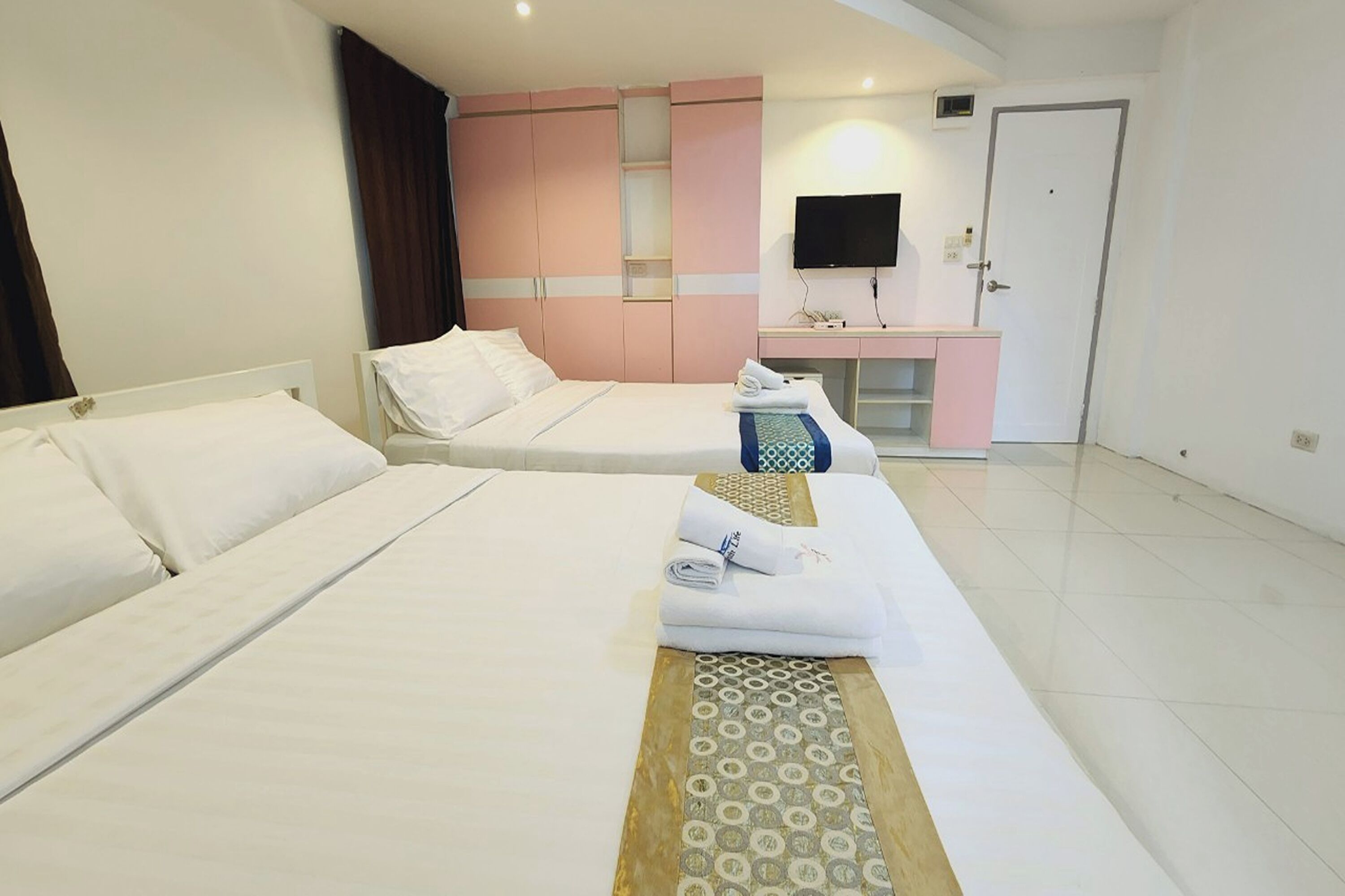 A hotel room with two beds, a flat-screen TV, a desk, and a door.