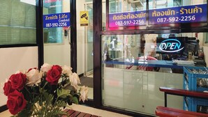 A hotel entrance with a glass door, a signboard with contact information, and a flower arrangement outside. - Zenith Life (Nonthaburi)