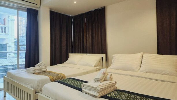 A hotel room with two beds, a window with curtains, and a radiator. - Zenith Life (Nonthaburi)