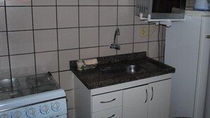 A compact kitchen with a stove, sink, microwave, and cabinets. - Apartment diRoma Fiori - Achei Férias (Caldas Novas)