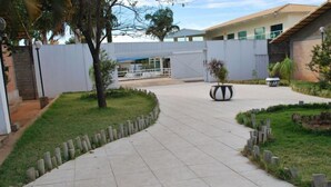 A paved pathway leading to a building with a modern design, surrounded by a well-maintained lawn and a few trees. - Apartment diRoma Resort - Achei Férias (Caldas Novas)