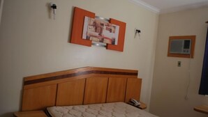 A hotel room with a wooden headboard, a bed with a quilted mattress, a bedside table, a wall-mounted telephone, and a framed picture above the bed. - Apartment diRoma Resort - Achei Férias (Caldas Novas)