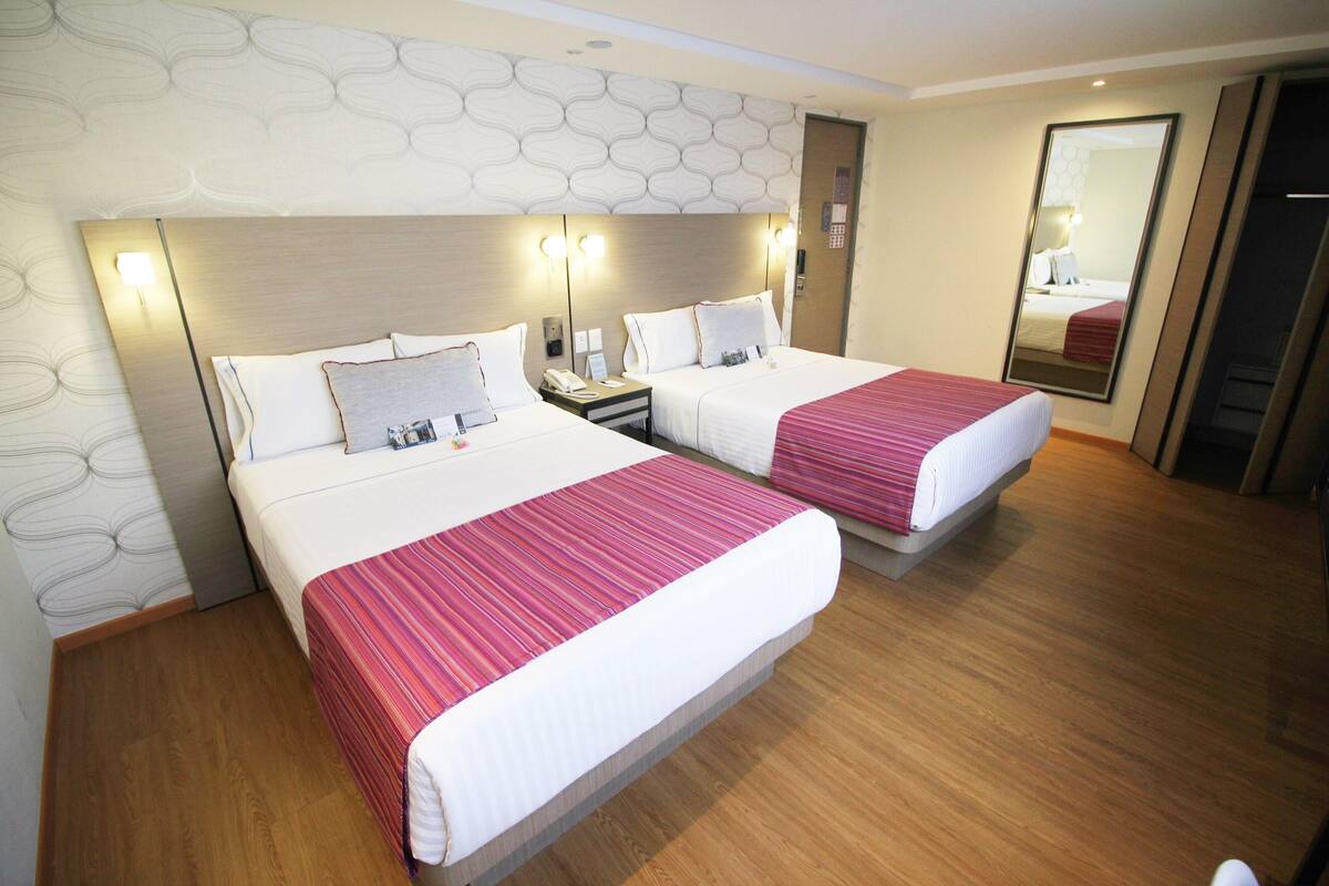 A hotel room with two beds, wooden flooring, and a patterned wall.