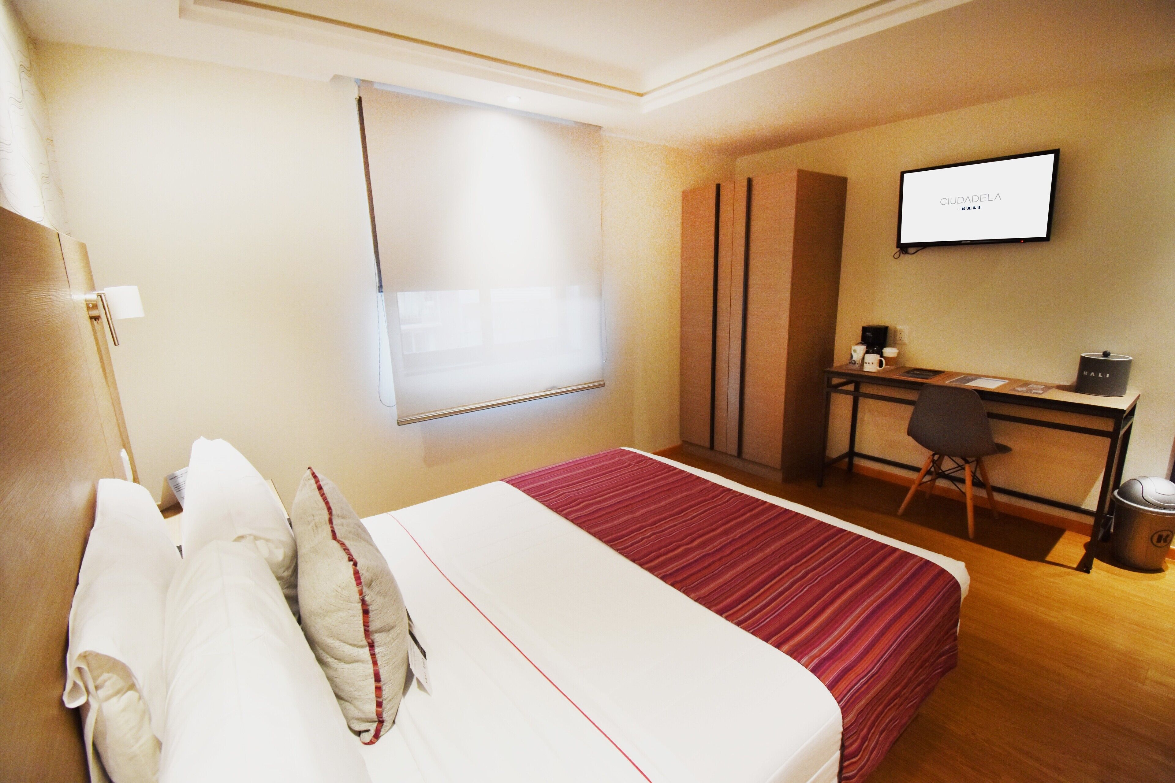 Une chambre d’hôtel avec un lit, un bureau, une chaise, une télévision et une fenêtre.