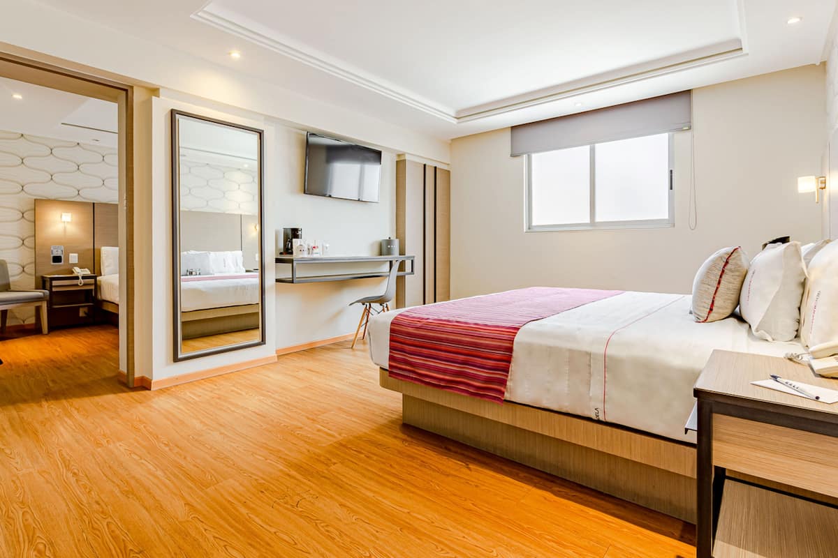 A modern hotel room with a large bed, a desk, a TV, and a bathroom with a mirror and toilet.