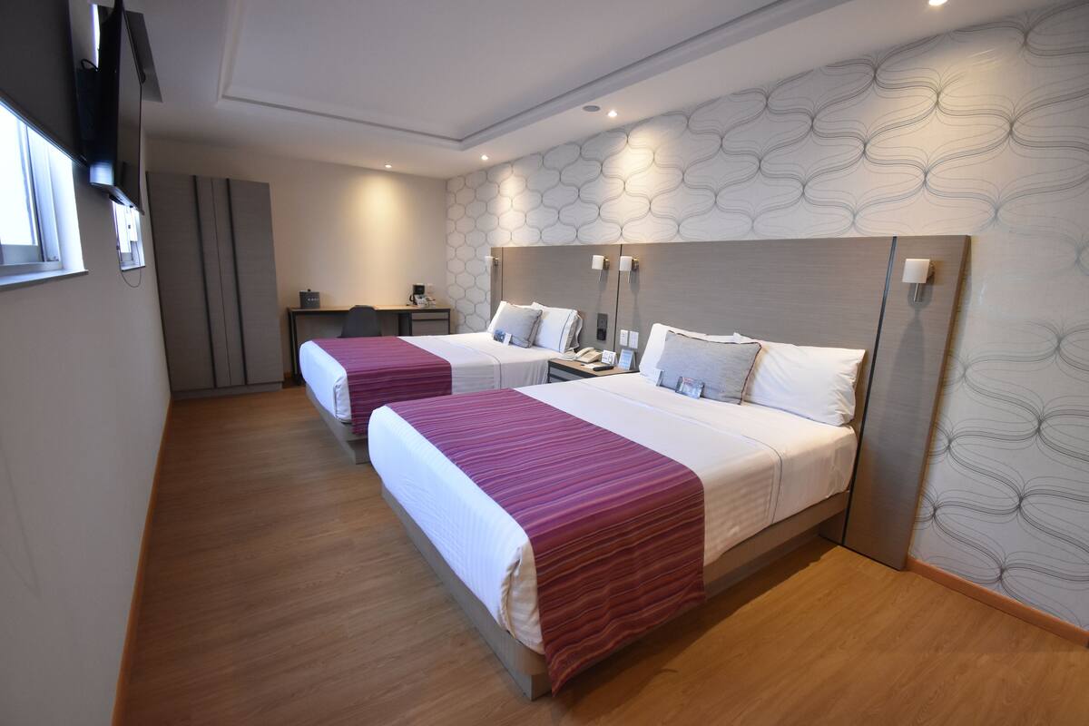 A hotel room with two beds, a desk, and a TV.