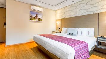 Une chambre d’hôtel moderne dotée d’un grand lit, d’un plancher en bois, d’un panneau décoratif au mur, d’un climatiseur et d’une table de chevet avec une lampe.
