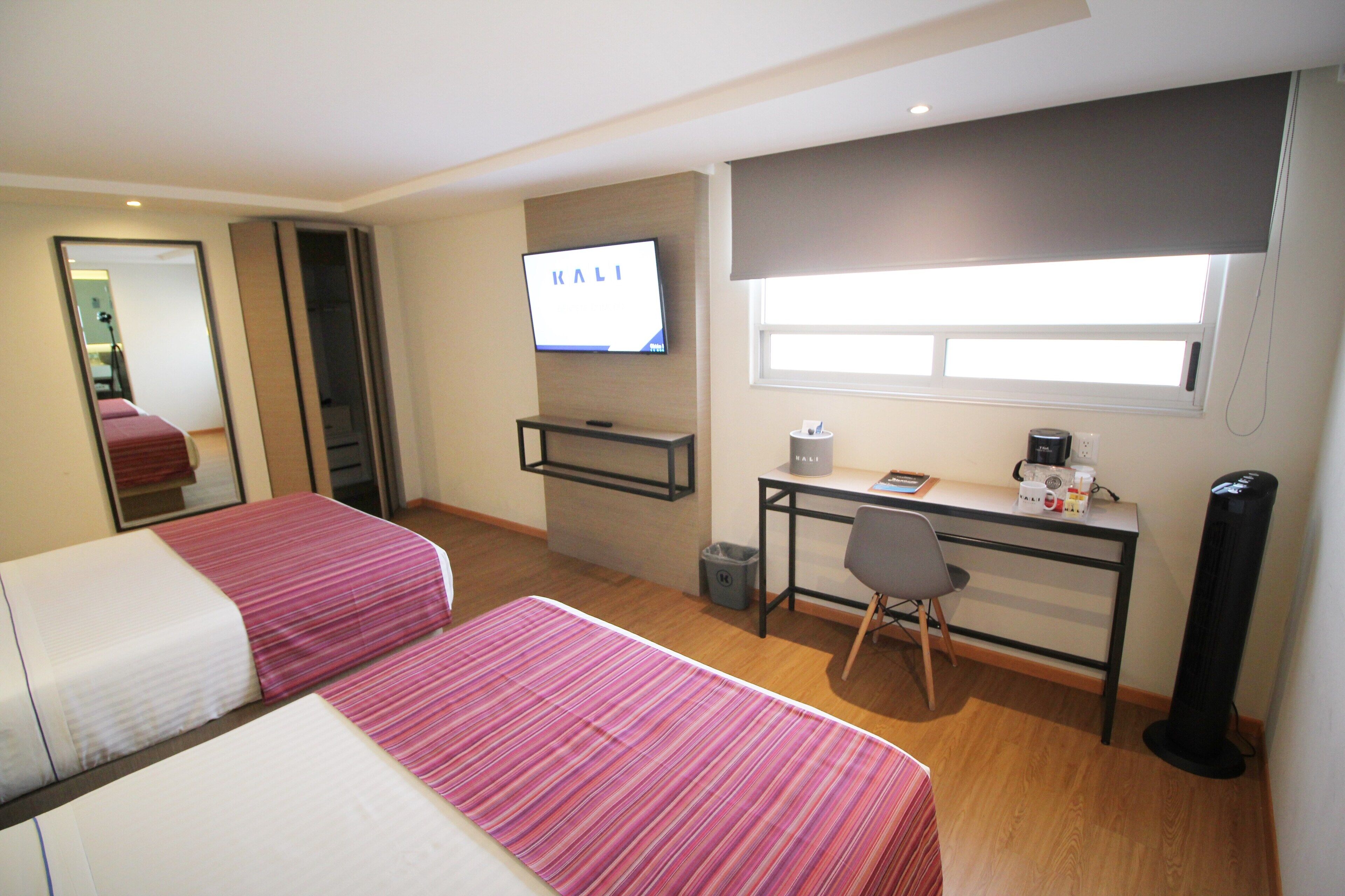 A hotel room with two beds, a desk, a chair, a TV, and a window.