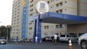 Un hotel con un logotipo destacado, varios pisos y un estacionamiento con varios automóviles.