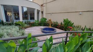 Un patio con piscina, rodeado de exuberante vegetación y un edificio moderno con grandes ventanales.