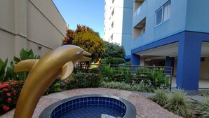 Una piscina con una escultura de delfín, rodeada por un patio con baldosas y follaje.