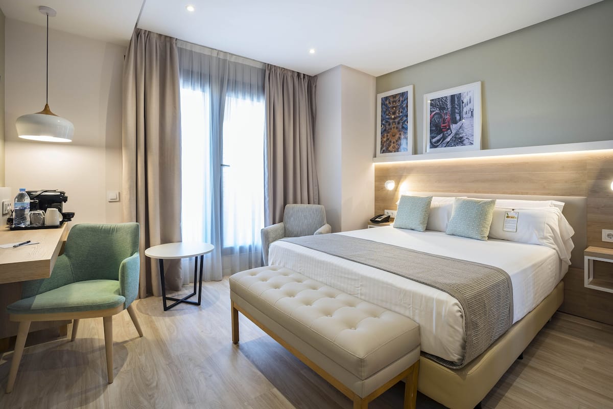 Une chambre d’hôtel moderne équipée d’un grand lit, d’un bureau, d’une chaise et d’un banc.