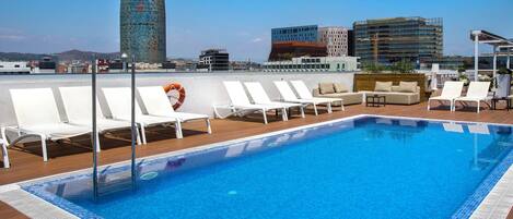 Una piscina sul tetto con poltrone da relax bianche, un galleggiante salvagente e uno skyline urbano con edifici moderni sullo sfondo.