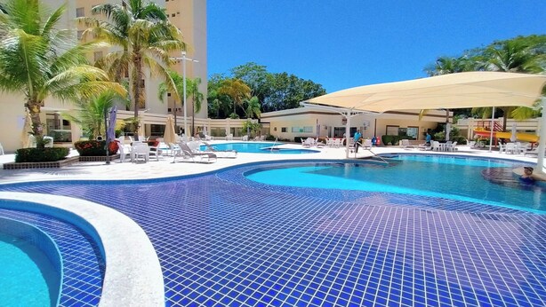 A resort pool area with multiple pools, lounge chairs, and palm trees. - Royal Residence - Achei Férias (Caldas Novas)