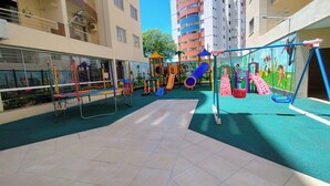 A playground area with various play structures, a covered seating area, and a view of surrounding buildings. - Royal Residence - Achei Férias (Caldas Novas)