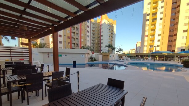 An outdoor patio area with tables and chairs, a pool, and high-rise buildings in the background. - Vitória das Thermas - Achei Férias (Caldas Novas)