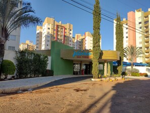 A hotel entrance with a green facade, palm trees, and a clear blue sky. - Vitória das Thermas - Achei Férias (Caldas Novas)
