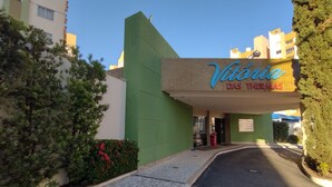 The entrance to a hotel named 'Victoria DAS THERMAS' with a green facade, a tiled pathway, and a clear sky. - Vitória das Thermas - Achei Férias (Caldas Novas)