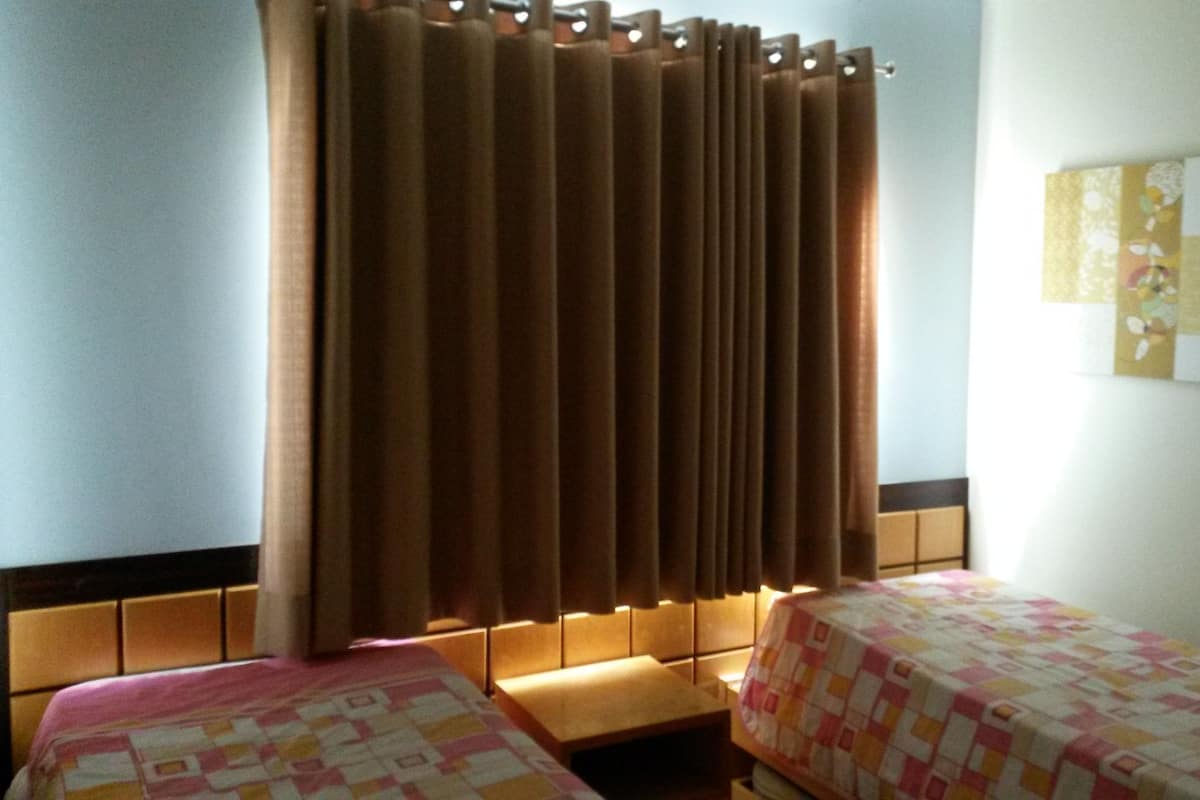 A hotel room with two beds, a curtain, and a wall-mounted quilted panel.