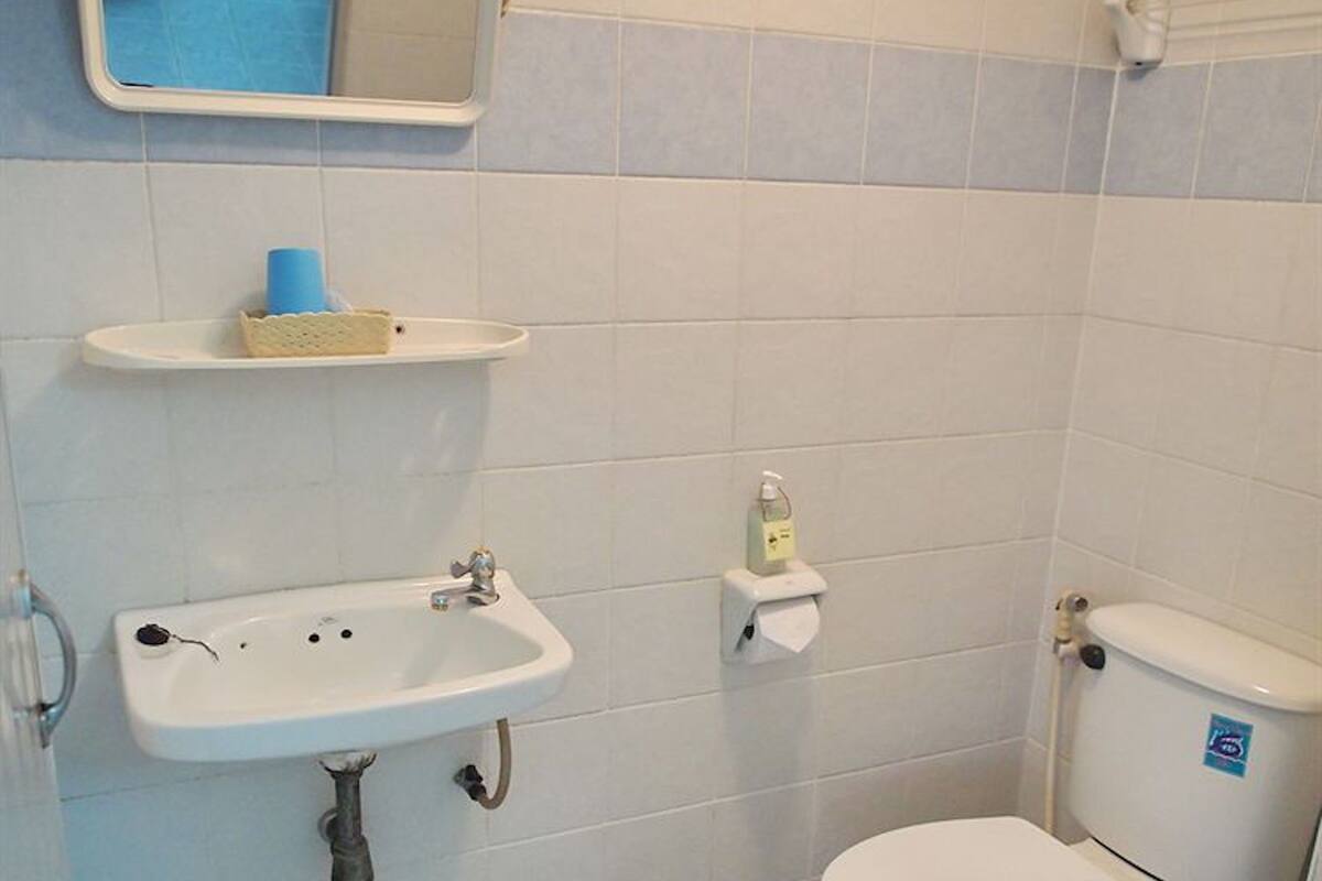 A small bathroom with a sink, toilet, and a mirror. There is a shelf above the sink and a trash bin next to the toilet.