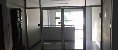 Un pasillo con un reloj, una puerta corrediza de vidrio y vista a otra habitación.