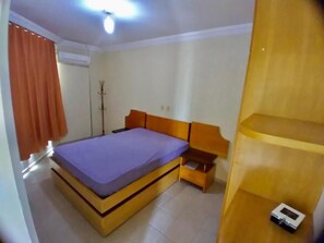 Une chambre à coucher comprenant un lit, une table de chevet en bois, une armoire et une lampe sur pied.