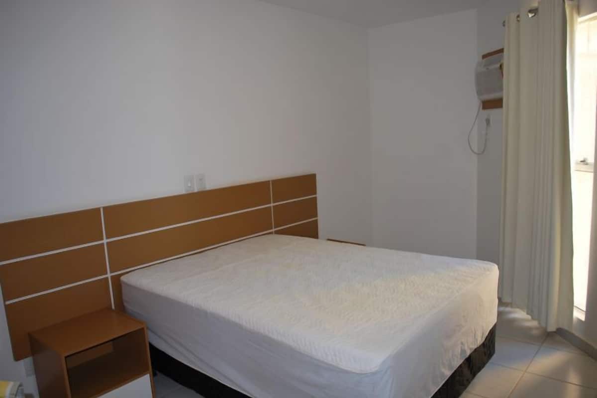 Een slaapkamer met een bed, nachtkastje en raam met gordijnen.