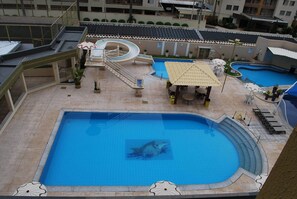 A swimming pool with a slide and a sun umbrella, surrounded by lounge chairs and potted plants.