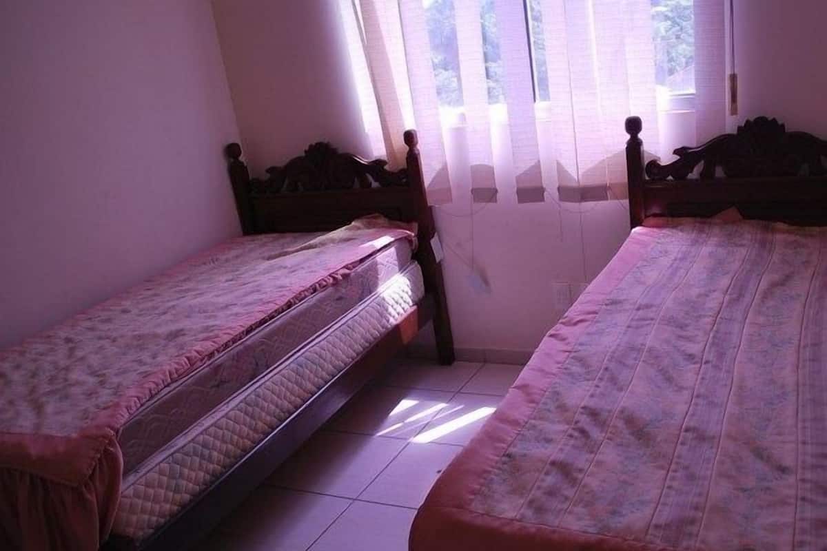 A room with two single beds, a window with sheer curtains, and a tiled floor.