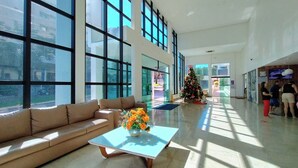 A spacious lobby with large windows, a beige sofa, a coffee table with flowers, and a decorated Christmas tree.