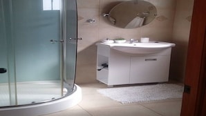 A modern bathroom with a glass-enclosed shower, a white sink, and a round mirror. - Cabaña Rústica Cristian Paihuano (Paiguano)