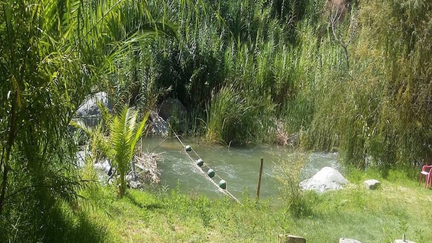 A natural outdoor area with a small stream, rocks, and a wooden bridge. - Cabaña Rústica Cristian Paihuano (Paiguano)