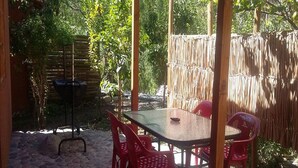 A covered outdoor patio with a table and chairs, surrounded by a bamboo fence and greenery. - Cabaña Rústica Cristian Paihuano (Paiguano)