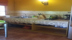 A kitchen with a sink, stove, and a green kettle on the counter. - Cabaña Rústica Cristian Paihuano (Paiguano)