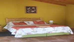 A bedroom with a wooden bed frame, a floral bedspread, and a nightstand with a lamp. - Cabaña Rústica Cristian Paihuano (Paiguano)