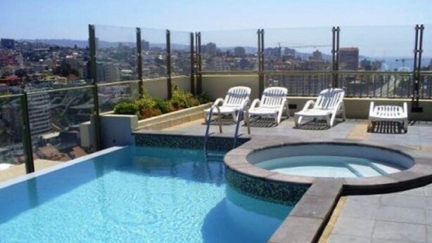 A rooftop pool with clear blue water, surrounded by white lounge chairs and a glass balustrade.