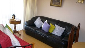 A living room with a black leather sofa, a wooden chair, a small round table, and a red chair with a white cushion.