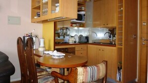 A compact kitchen with wooden cabinets, a dining table with chairs, and a microwave.