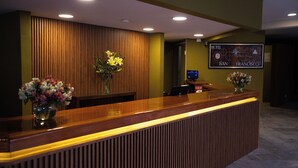 Un mostrador de recepción de hotel con detalles de madera, dos arreglos florales y un letrero en la pared que indica la ubicación del hotel en San Francisco.