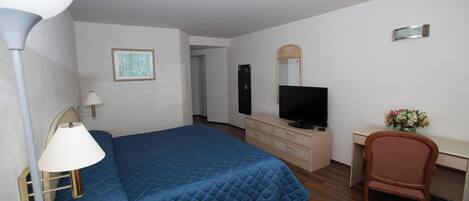 Une chambre d’hôtel équipée d’un lit, d’un bureau, d’une chaise, d’une télévision, d’une lampe et d’un vase à fleurs.