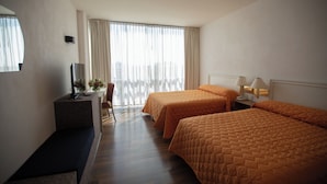 Habitación de hotel con dos camas, un escritorio, un televisor, una silla y una ventana con cortinas.