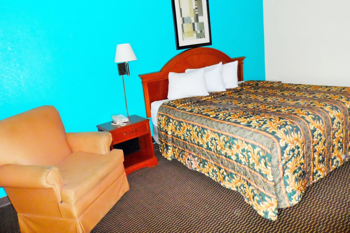 A hotel room with a bed, a nightstand, a lamp, and a chair.