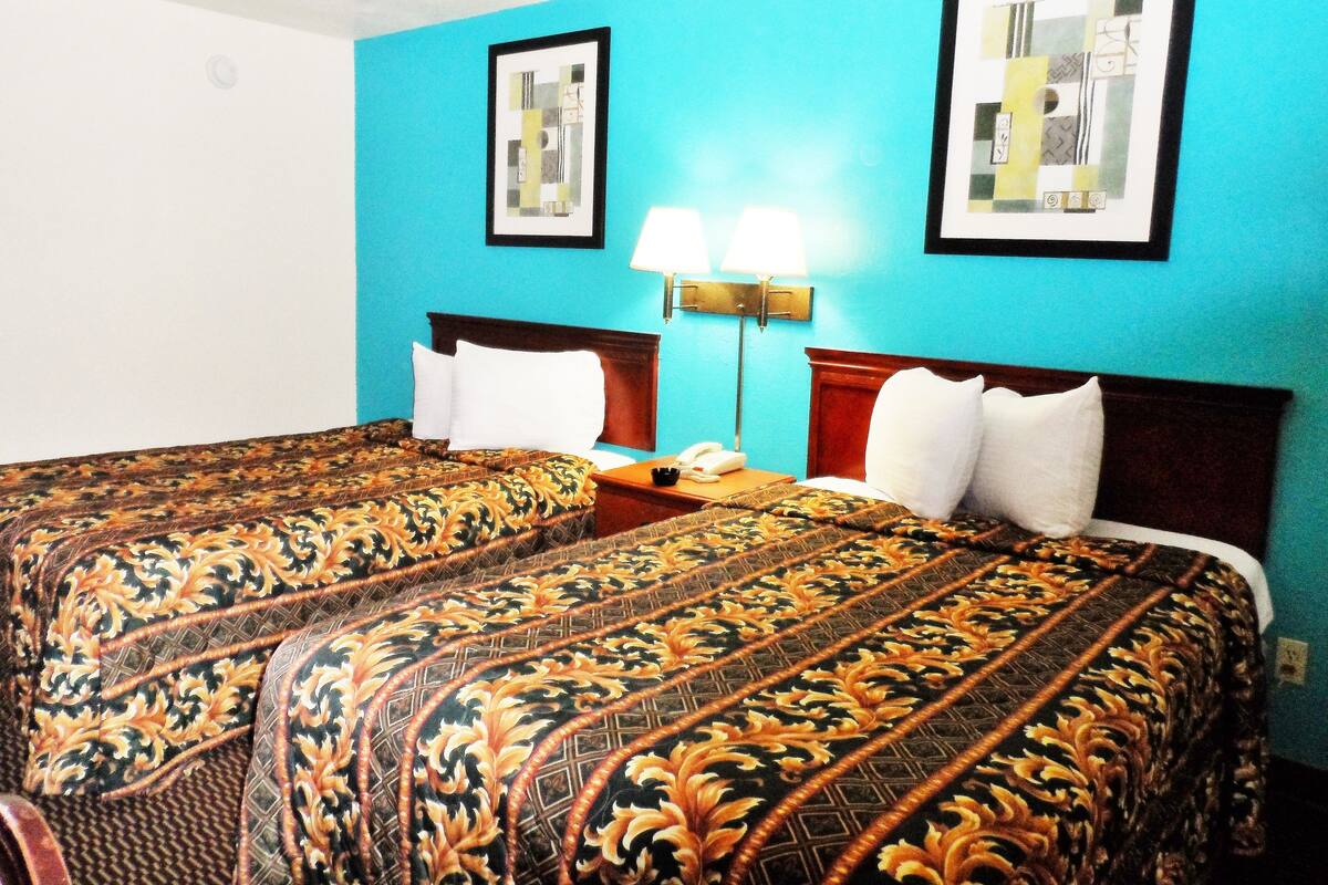 A hotel room with two beds, a nightstand, and two wall-mounted lamps.
