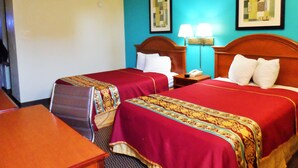 A hotel room with two beds, a desk, and a chair. There are two bedside tables with lamps and a telephone. The walls are painted in two colors, and there are two framed pictures on the wall. - Courtesy Inn (Oklahoma City)
