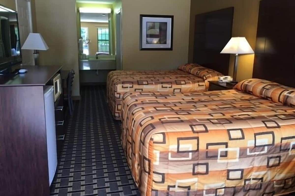 A hotel room with a bed, a desk, a chair, a lamp, and a framed picture on the wall.