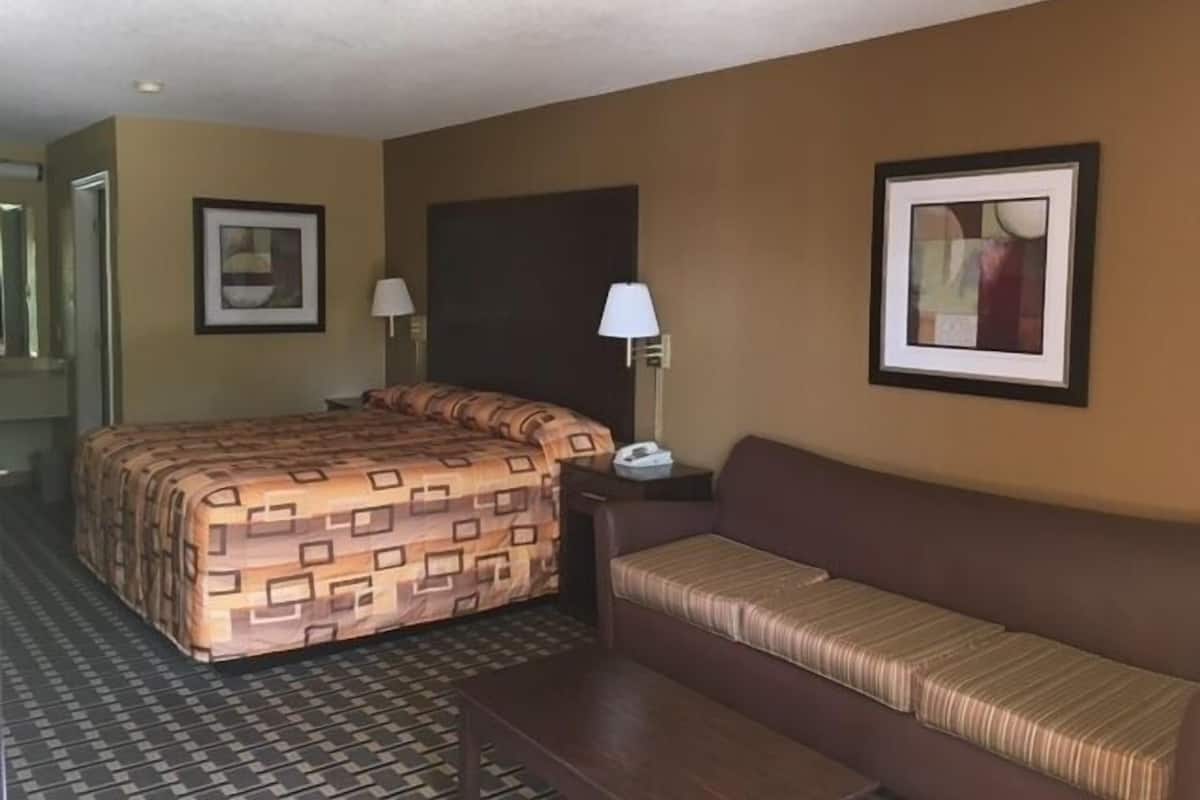 A hotel room with a bed, a sofa, a nightstand, two wall lamps, and framed artwork.