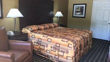 A hotel room with a bed, two bedside lamps, a chair, a nightstand, a door, and a framed picture on the wall.