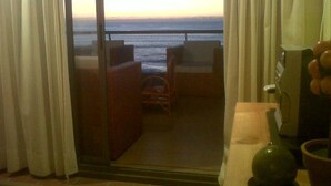 A balcony with a view of the sea, a chair, and a table.