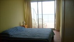 A bedroom with a bed, a nightstand, and a view of the beach through the window.